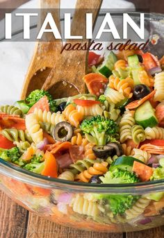 a pasta salad in a glass bowl with a wooden spoon and serving utensils