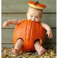 a baby in a pumpkin costume sitting on the ground