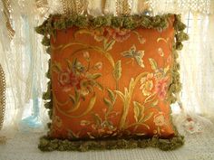 an orange pillow with flowers on it sitting on a white lace doily covered table