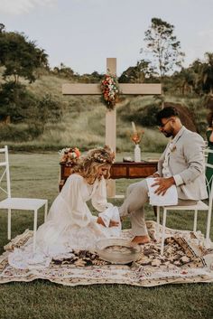 a bride and groom are sitting on a blanket at the alter in front of a cross