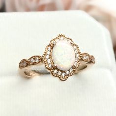 an opal and diamond ring sits on a white cloth with a rose in the background