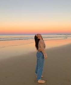 a woman standing on top of a sandy beach next to the ocean at sunset with her eyes closed