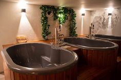 a large bath tub sitting next to two sinks in a room with plants growing on the wall