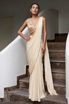 Beige pre-draped plain saree with nalki, pearl beads embellished border. Paired with sleeveless V neck padded blouse with nalki, pearls, stones, crystals, sequin floral clusters embroidery.
Components: 2
Pattern: Embroidery
Type Of Work: Nalki, Pearls, Stones, Crystals, Sequin
Neckline: V Neck
Sleeve Type: Sleeveless
Fabric: Viscose Georgette Satin, Lining: Shantoon
Color: Beige
Other Details: 
Attached inner lining
Padded blouse
Weight: 0.5kgs
Length: 42inches
Model Height: 5ft 8inches, wearing South Indian White Sari Look, Beige Saree Party Wear, Party Sarees Elegant, Beige Saree Look, Sari Inspired Wedding Dress, V Neck Blouse Indian Sleeveless, Plain Saree Look, Halter Blouse Saree, Simple Plain Saree