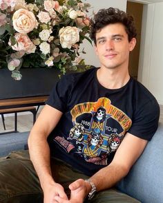 a man sitting on a couch in front of a vase with roses and other flowers