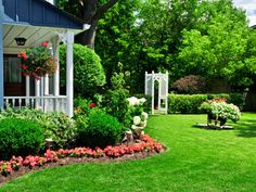 a garden with flowers and statues in the grass next to a blue house on a sunny day