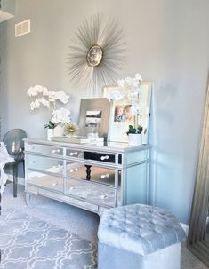 a silver dresser sitting in a living room next to a white chair and mirror on the wall