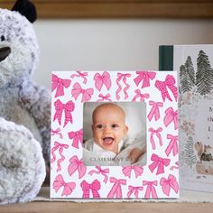 a teddy bear sitting next to a pink and white photo frame with a baby's name on it