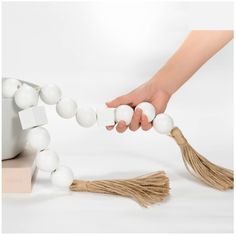 a hand reaching for some white balls on a string with tassels around it