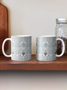 two coffee mugs sitting on top of a wooden shelf next to a mason jar