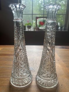 two clear glass vases sitting on top of a wooden table next to a window