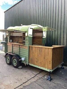 an old green trailer is parked in front of a building with a awning on the roof