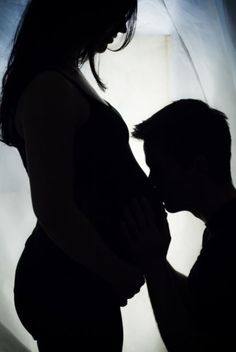 the silhouette of a pregnant woman holding her baby bumping it's belly in front of a sheer curtain