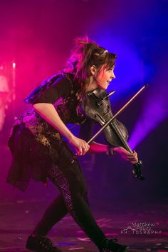 a woman playing the violin on stage with purple lighting behind her and black tights