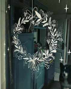 a black and white dog standing in front of a glass door with a wreath drawn on it