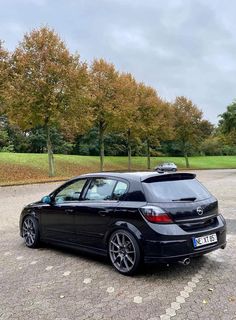 a black car parked in a parking lot next to some trees and grass on a cloudy day