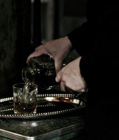 a person pouring tea into a glass on top of a metal tray with two cups