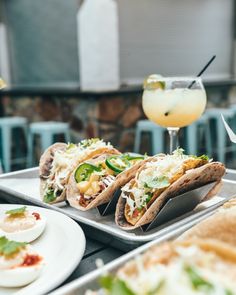 several tacos and drinks are sitting on a tray at a table with other food items