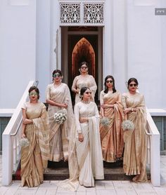 a group of women standing next to each other in front of a door wearing sari