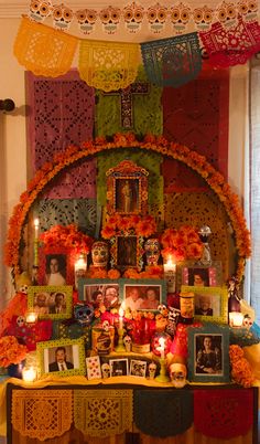 a table with pictures and candles on it in front of a wall decorated with mexican decorations