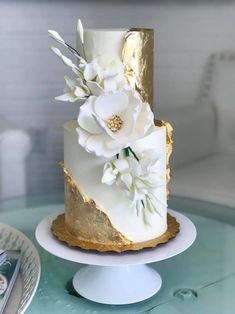 a white and gold wedding cake with flowers on top