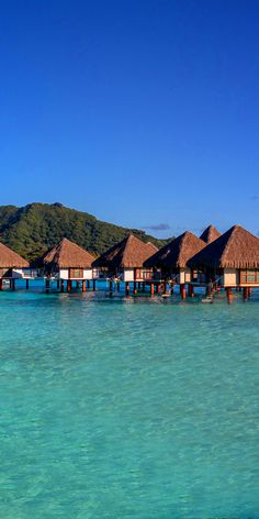 the water is crystal blue and clear with some huts on it's sides in the ocean