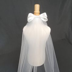 Simple one-tier cut-edge veil with added 6 inch satin bow, ideal for first communion or bachelorette.  Tulle is 54 inches wide so the veil is suitable for children or adults. Length is 20 inches. *This is a petite veil, primarily intended for communion. On an adult, the length is just below the shoulder. Shown on a child's body form. The veil is attached to a clear comb. I can accommodate customizations such as different lengths, embellishments, or barrettes with a slightly extended production t First Communion Tulle Dress With Satin Bow, Tulle First Communion Dress With Satin Bow, White First Communion Dress With Satin Bow For Party, First Communion Satin Dress With Satin Bow, Satin First Communion Dress With Satin Bow, White Tulle First Communion Dress With Bow, Cream Ribbon Wedding Bow, Elegant First Communion Dress With Tulle Bow, Elegant Fitted First Communion Dress With Satin Bow