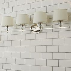 a bathroom light fixture with four lamps on the side of it against a white brick wall