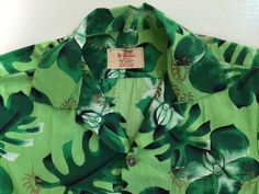 "This is a beautiful, mid century Hawaiian shirt. The hand screen painted design depicts orchids and tropical leaves in green, white, black, and gold. It is 100% cotton and made in Hawaii. The colors are so vibrant and the shirt so crisp, it makes me think that it may even be deadstock. It is in excellent vintage condition except for a missing Chinese coin button at the last button hole and a tiny hole under the pocket.   Measurements: Chest: 43\" Shoulder width: 16 1/2\" CB length: 27 1/2\"" Cheap Green Hawaiian Shirt, Cheap Green Retro Hawaiian Shirt, Green Tropical Printed Shirt, Green Cotton Shirt With Tropical Print, Green Printed Tropical Camp Shirt, Tropical Printed Green Camp Shirt, Green Floral Print Hawaiian Shirt, Green Tropical Print Hawaiian Shirt, Tropical Green Printed Camp Shirt