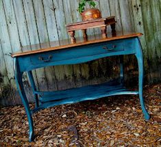 an old blue table with a potted plant on top is in front of a wooden fence