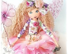 a doll with blonde hair sitting on top of a pink flowered dress and butterfly wings