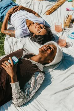 two people laying on the ground with food and drinks in their hands while one person holds an object up to his ear