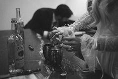 two people are sitting at a table with bottles and glasses on it, one person is pouring something into the cup