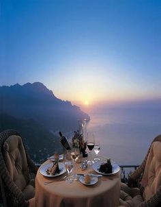 the table is set for two with wine and cheese on it, overlooking the ocean