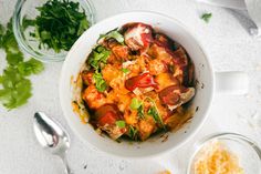 a white bowl filled with lots of food next to other bowls and utensils