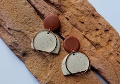 two brown and white earrings sitting on top of a rock