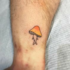 a small mushroom tattoo on the ankle with an orange and yellow hued hat underneath it