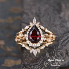 a gold ring with a red stone surrounded by white diamonds on top of a rock