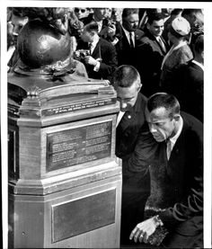 black and white photograph of men in suits looking at a monument with writing on it