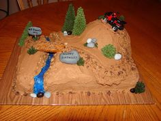 a birthday cake made to look like a mountain with a river running through it and cars driving on top