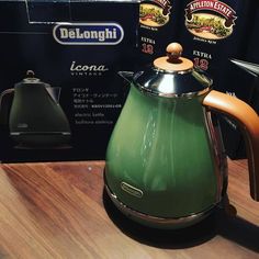 a green tea kettle sitting on top of a wooden table next to two boxes of delonghi