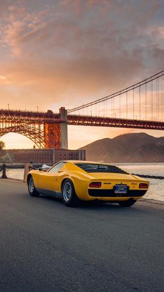 a yellow sports car is parked in front of the golden gate bridge at sunset or sunrise