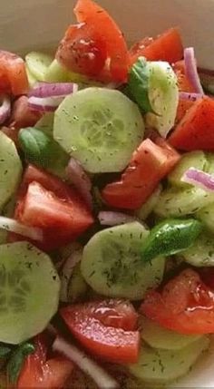 a salad with cucumbers, tomatoes and onions in a white bowl on a table