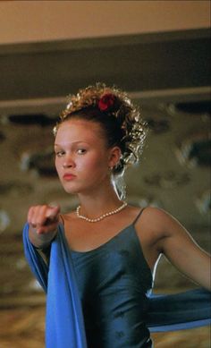 a woman in a blue dress and pearls is holding a blue scarf around her neck