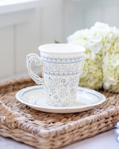 a coffee cup and saucer on a wicker tray with flowers in the background