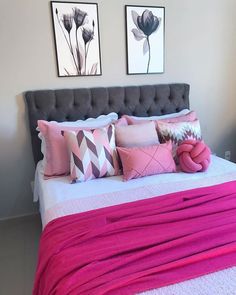 a bed with pink sheets and pillows in a bedroom next to two pictures on the wall