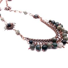 Warm tones of copper pair with varying shades of green moss agate to define this statement necklace. Varying handmade copper links are interspersed with handmade sun charms and are anchored by a beaded frame loaded with moss agate beads. Drop: 15" Frame: 3" across by 3" length Handmade in Lincoln, Nebraska Handmade Moss Agate Round Beads Necklace, Green Moss Agate Bohemian Jewelry, Bohemian Green Moss Agate Jewelry, Green Bohemian Moss Agate Jewelry, Green Bohemian Copper Wire Necklace, Bohemian Jade Necklace With Wire Wrapped Details, Bohemian Jade Necklace With Wire Wrapping, Bohemian Jade Necklace Wire Wrapped, Bohemian Jade Wire Wrapped Necklace