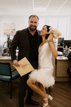 a man standing next to a woman in a white dress and feather skirt holding flowers