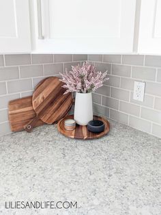 a white vase with flowers in it sitting on a wooden tray next to some cutting boards