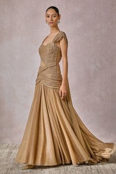 Champagne gold fluted gown with corsetted bodice in crystal, pearl embellishment and draped panel at the back. - Aza Fashions Gold Gown With Sweetheart Neckline For Evening, Festive Draped Fitted Evening Dress, Festive Fitted Draped Evening Dress, Gold Gown With Sweep Train And Fitted Bodice, Gold Fitted Dress For Reception, Fitted Evening Dress With Sweep Train For Reception, Gold Floor-length Evening Dress For Reception, Fitted Draped Gown For Reception, Gold Evening Gown With Sweetheart Neckline